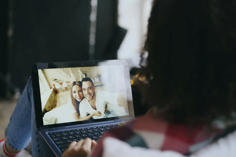 Mulher deitada na cama, em videochamada com amigos pelo notebook