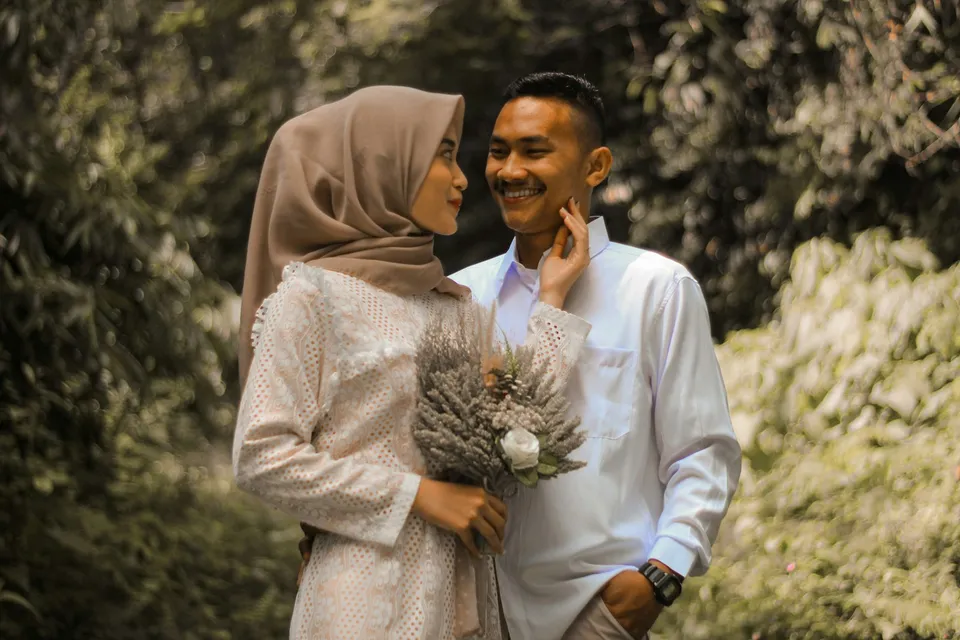 Perempuan berhijab memegang buket bunga kering dan tersenyum ke pasangannya di taman