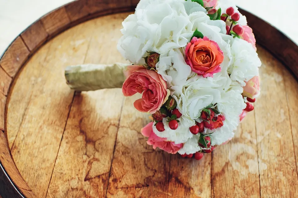 A bridal bouquet of white and coral flowers resting on a wooden barrel