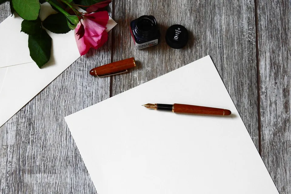 Una hoja en blanco, una pluma y una rosa sobre una mesa de madera