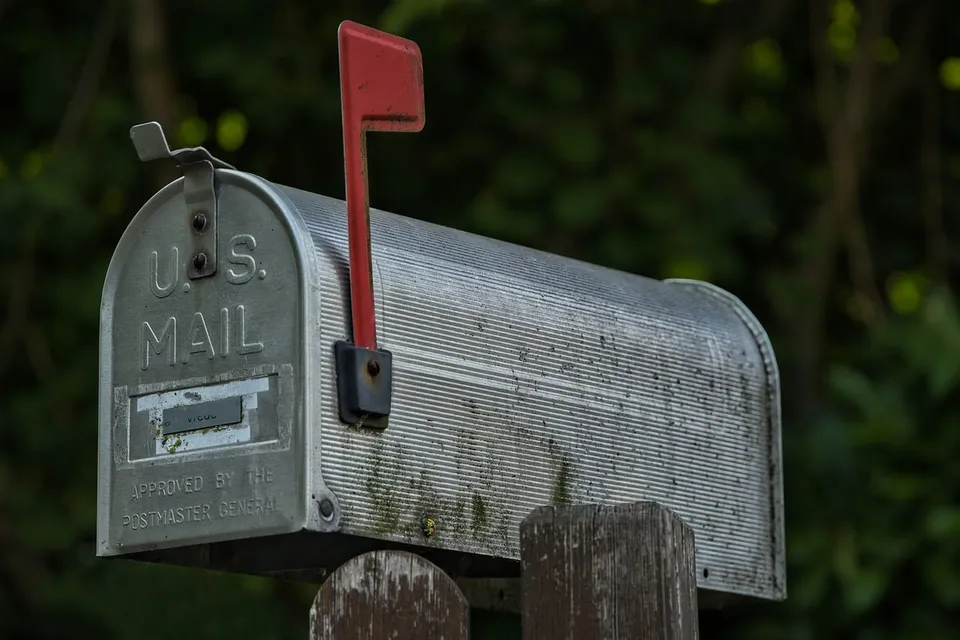 A metal U.S. Mail mailbox on a wooden post with its red flag up
