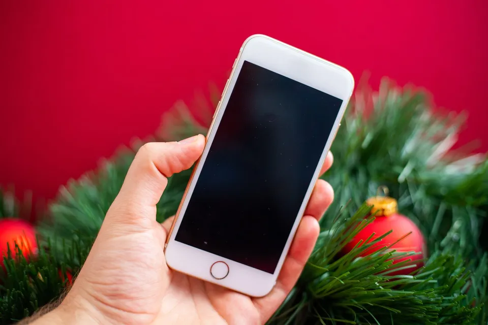 Uma mão segura um celular entre galhos de pinheiro e enfeites de Natal vermelhos