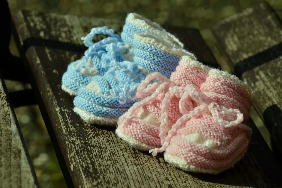 A pair of knitted baby booties, one pink and one blue, on a wooden bench
