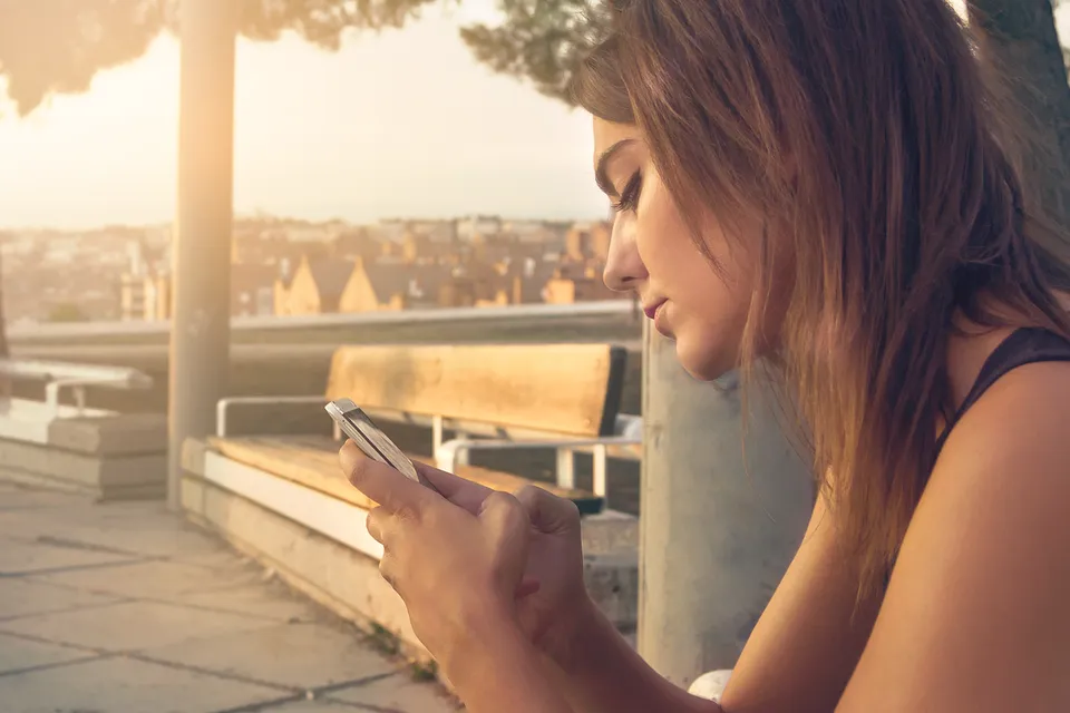 Una chica en una terraza al atardecer lee algo en su móvil, pensativa