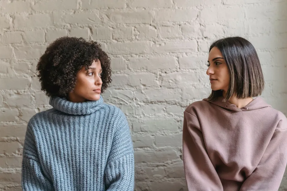 Dos amigas sentadas junto a una pared de ladrillo blanco se miran en silencio