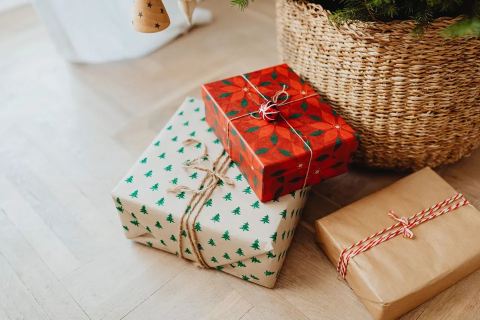 Regalos envueltos en papel de colores, apilados en el suelo junto a una cesta de mimbre