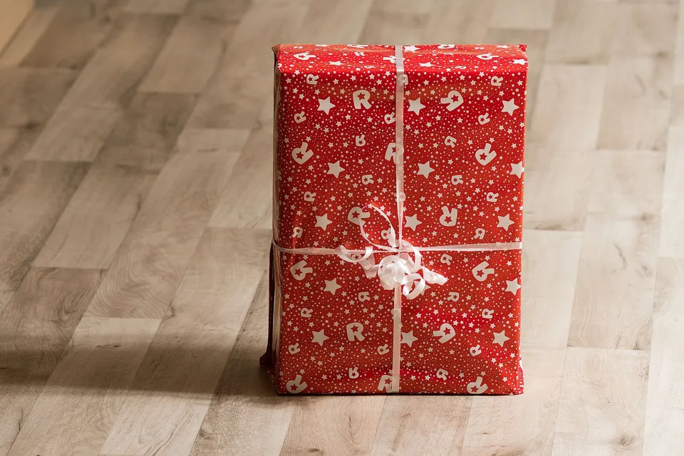 A gift box wrapped in red paper with a white ribbon on a wooden floor