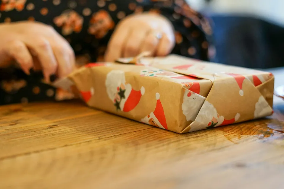 A person wrapping a present on a wooden table during a Secret Santa session
