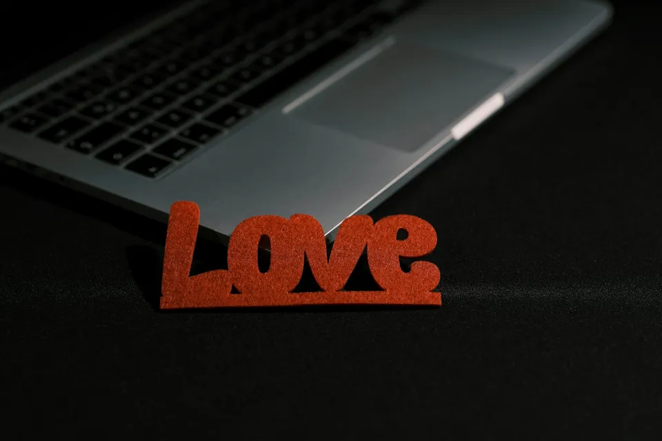A red “Love” sign leaning on an open laptop on a dark desk